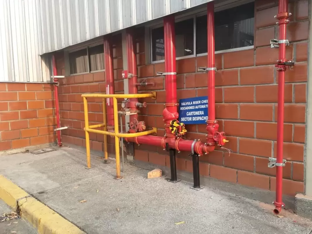 Sistema contraincendios en sector de despacho. Tuberías y válvulas rojas en pared de ladrillo.